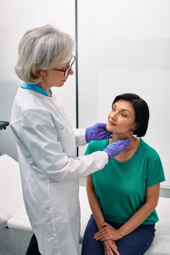 Woman endocrinologist palpates of woman's neck for diagnostics of thyroid diseases. Thyroid gland exam and treatment